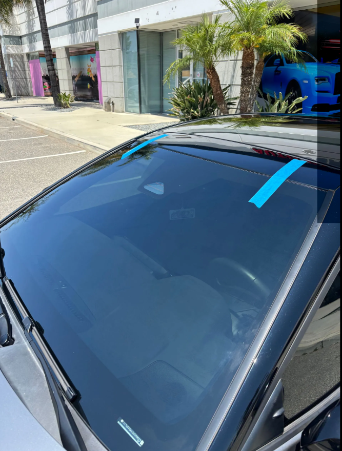 New windshield installed on a black sedan with blue retention tape holding the moulding